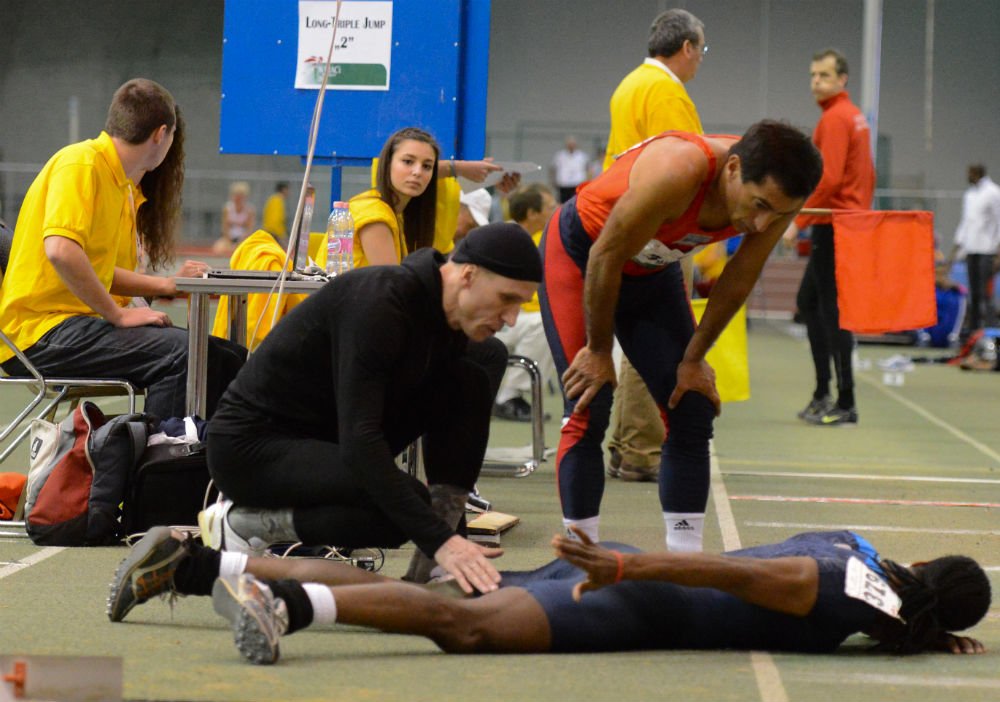 Karl Hawke checks on U.S. teammate Antonio after injury during triple jump.
